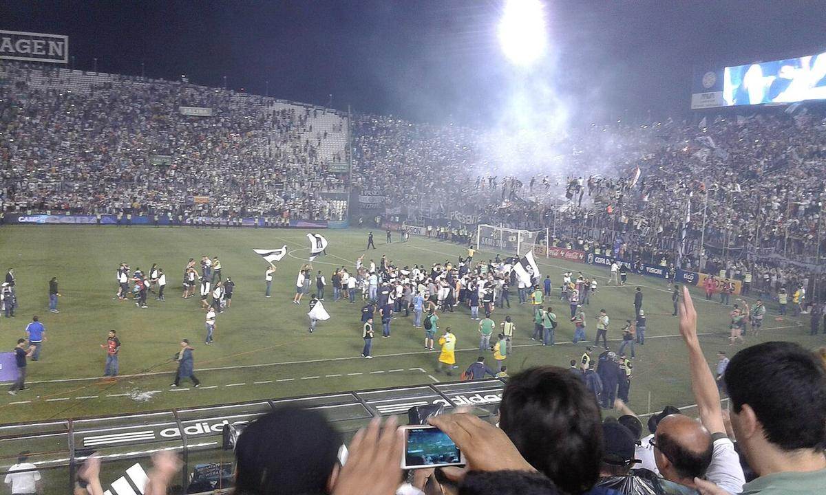 Jugadores de Olimpia celebrando un título en el campo, con la hinchada de fondo