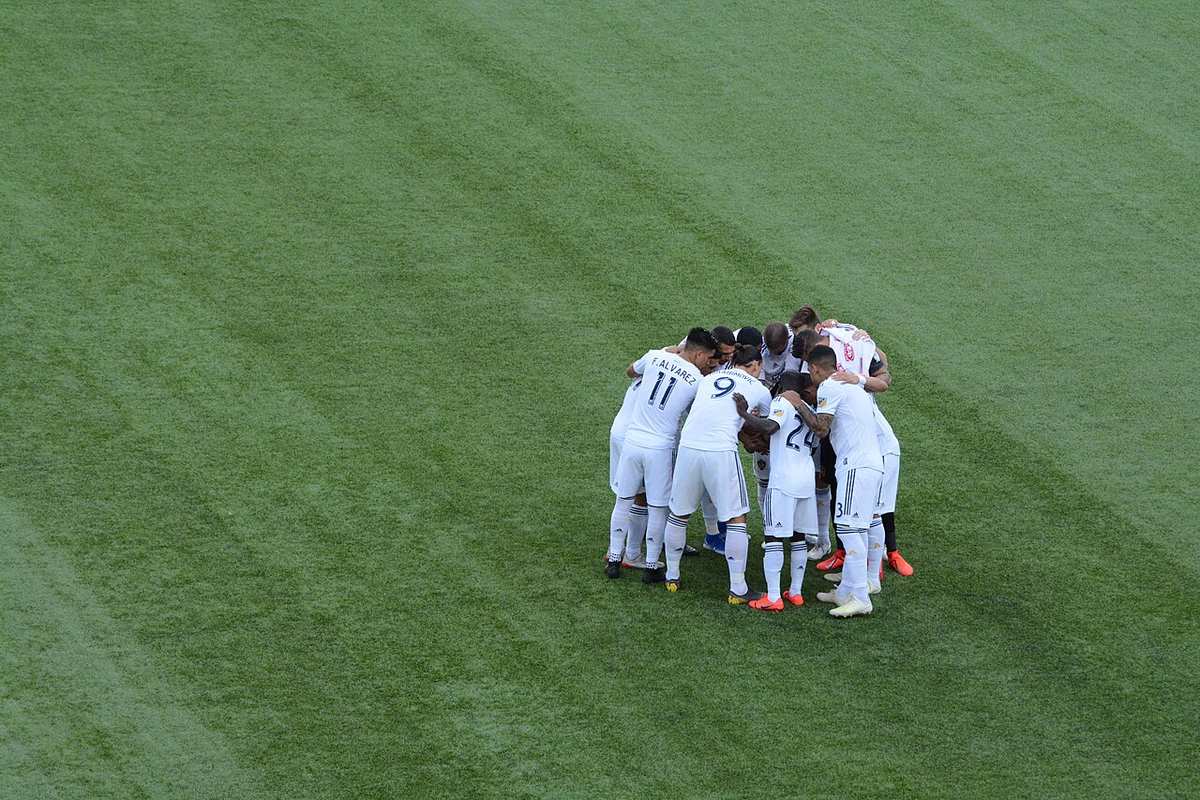 Jugadores de LA Galaxy reunidos en la cancha antes de un partido, con el estadio de fondo
