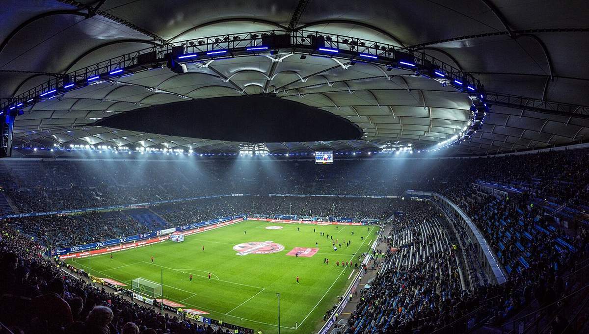 Un stade de football illuminé la nuit, avec une pelouse verte et des tribunes pleines